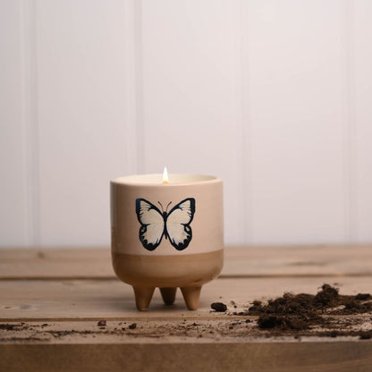 Candle in a pot with a butterfly design on a wooden surface