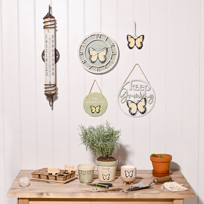 Decorative items including a clock, thermometer, and wall hangings with butterfly designs on a white wall.