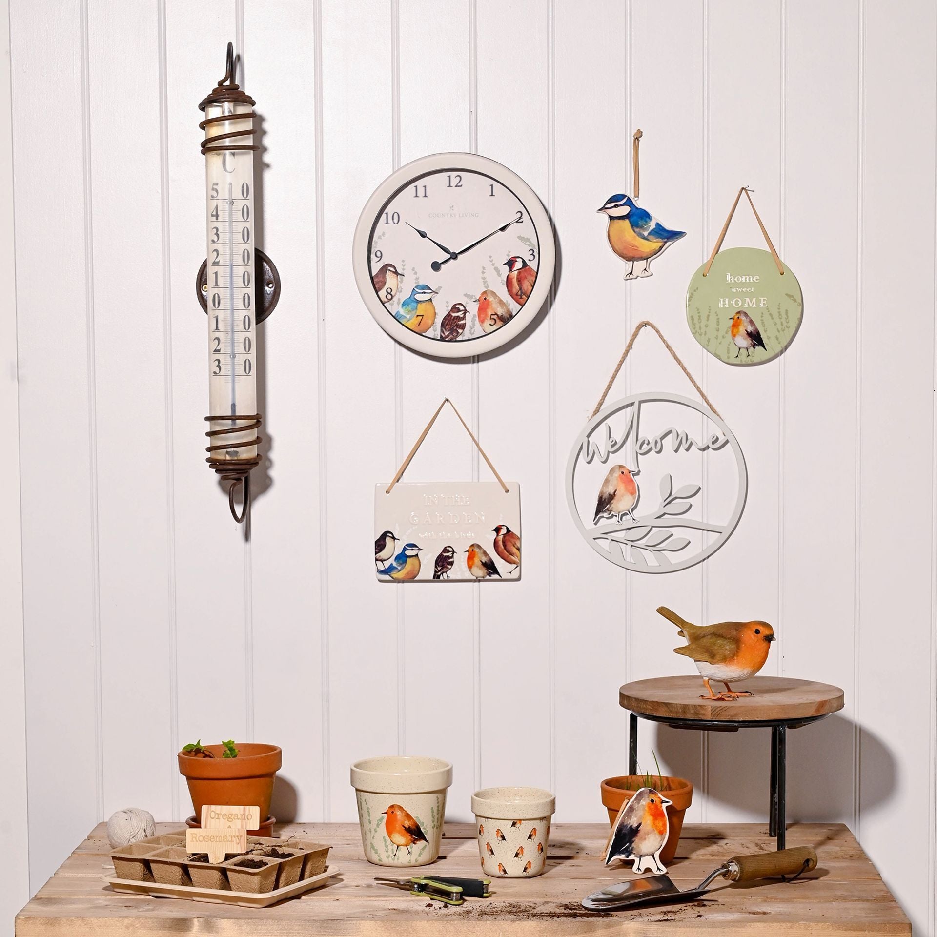 Decorative items including a clock, thermometers, and bird-themed wall art on a wooden surface with a white paneled background.