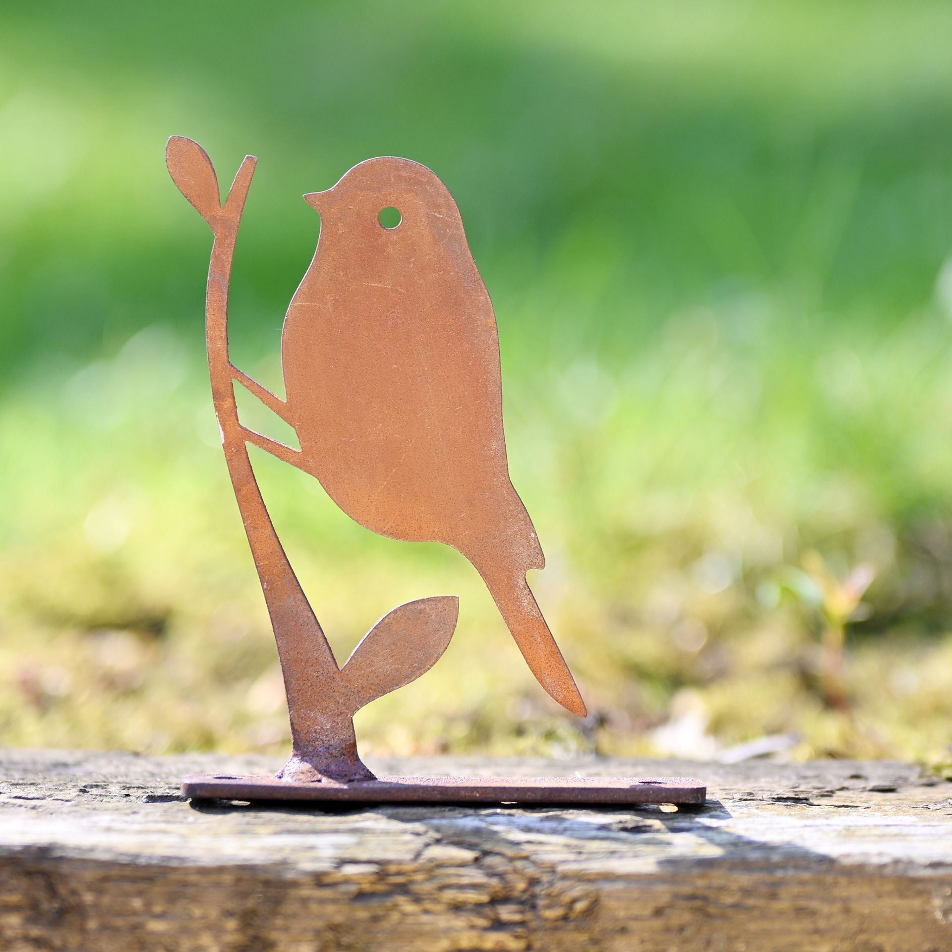 Metal bird sculpture on a wooden surface with a blurred green background