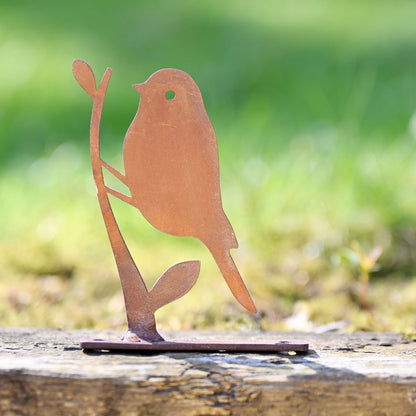 Metal bird sculpture on a wooden surface with a blurred green background