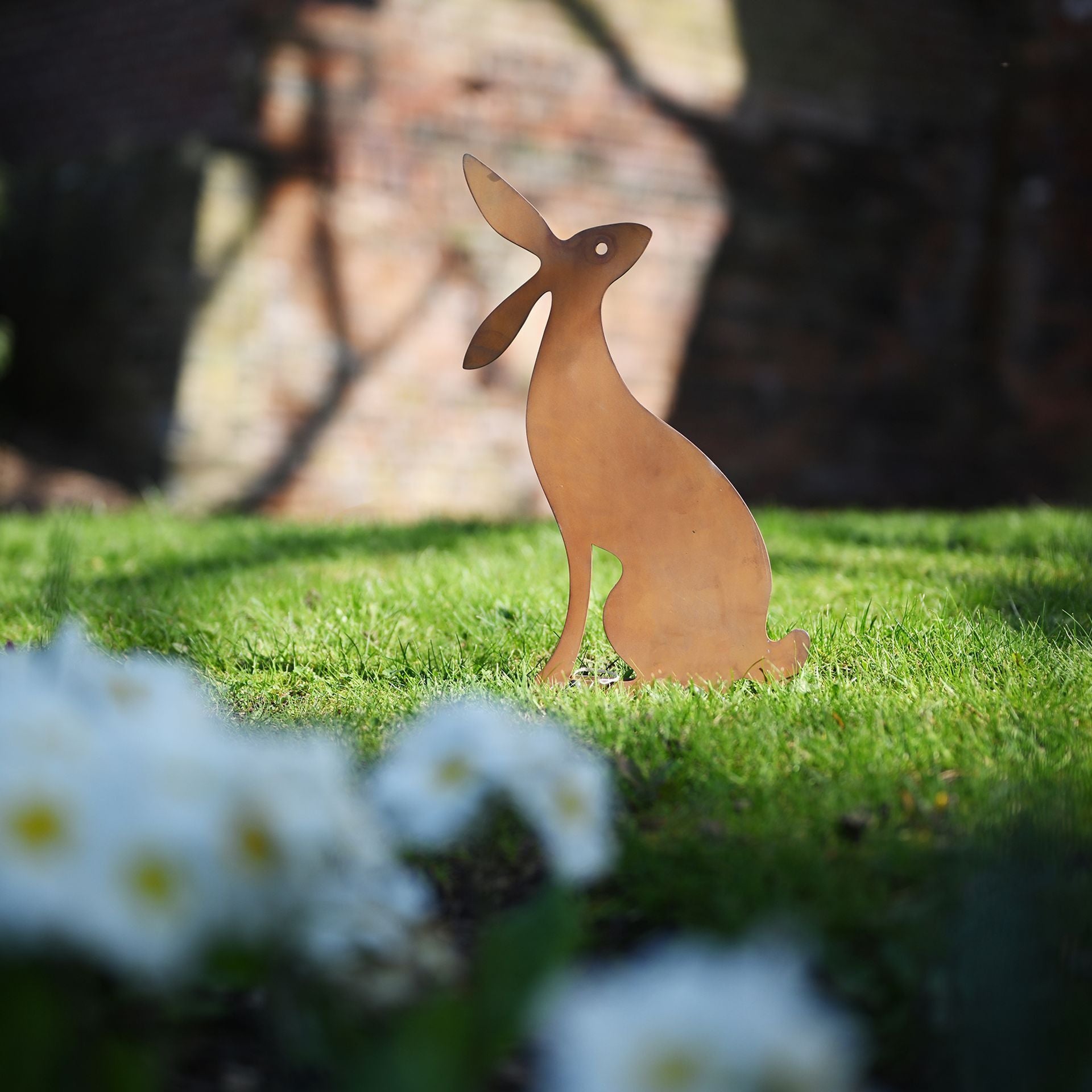 Metallic rabbit sculpture on grass with flowers and blurred background