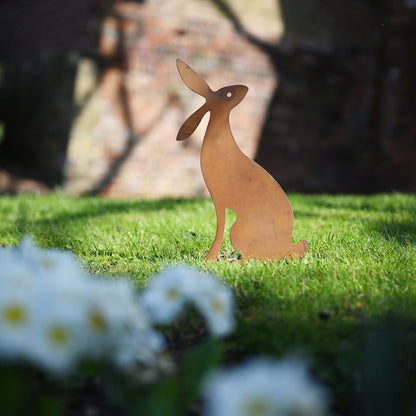 Metallic rabbit sculpture on grass with flowers and blurred background