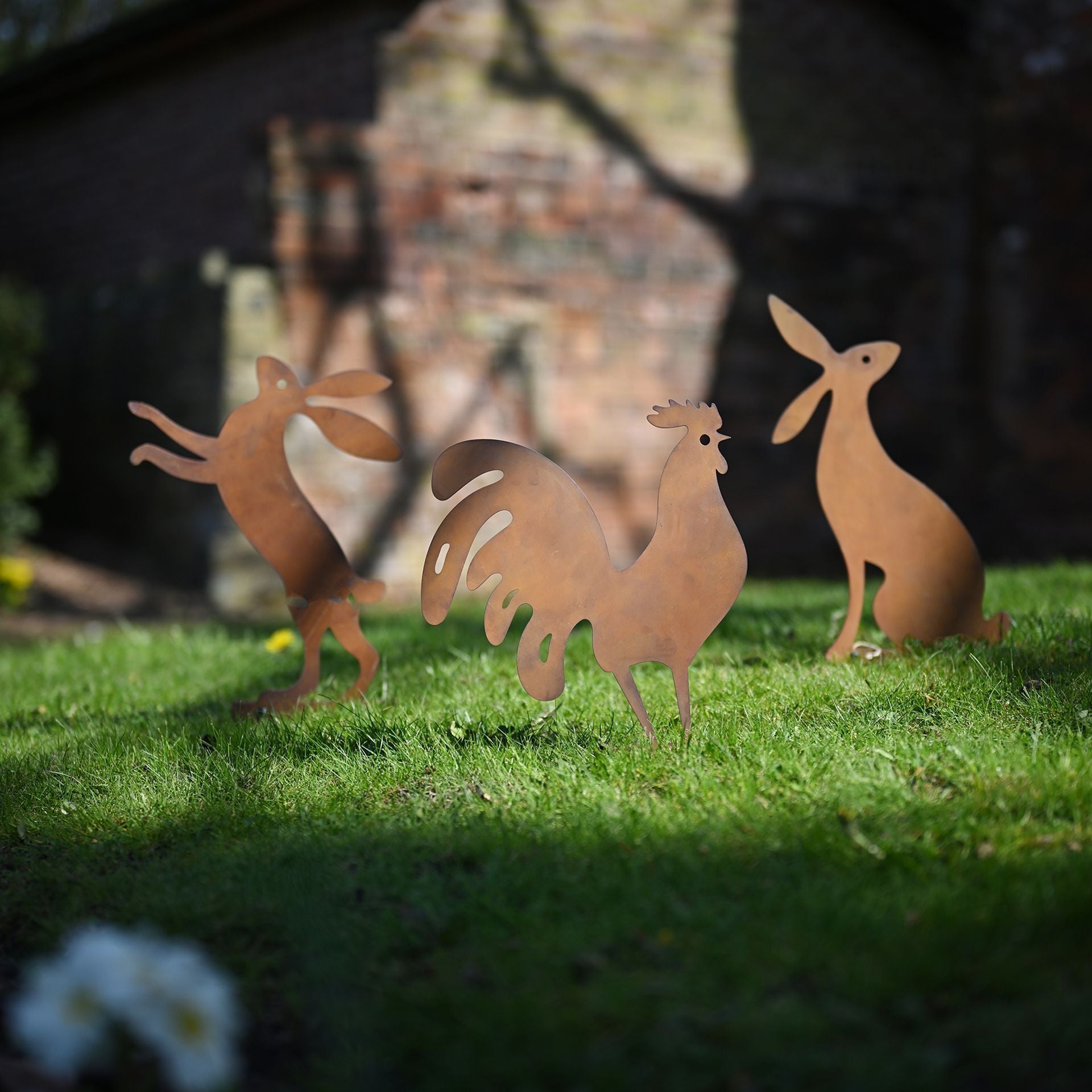 Metallic rooster sculptures on grass with a blurred background