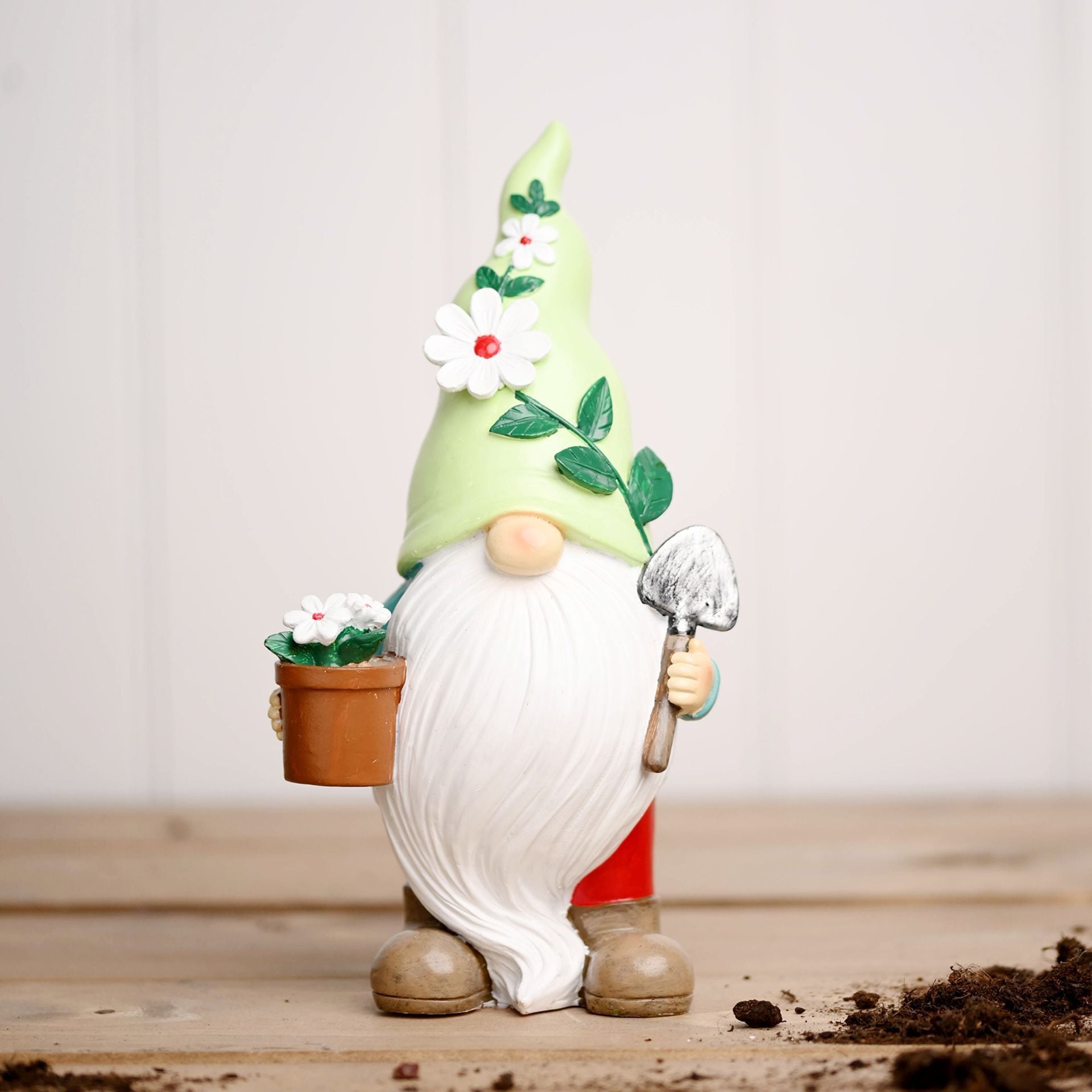 Gnome figurine holding a flower pot and a shovel on a wooden surface with a light background