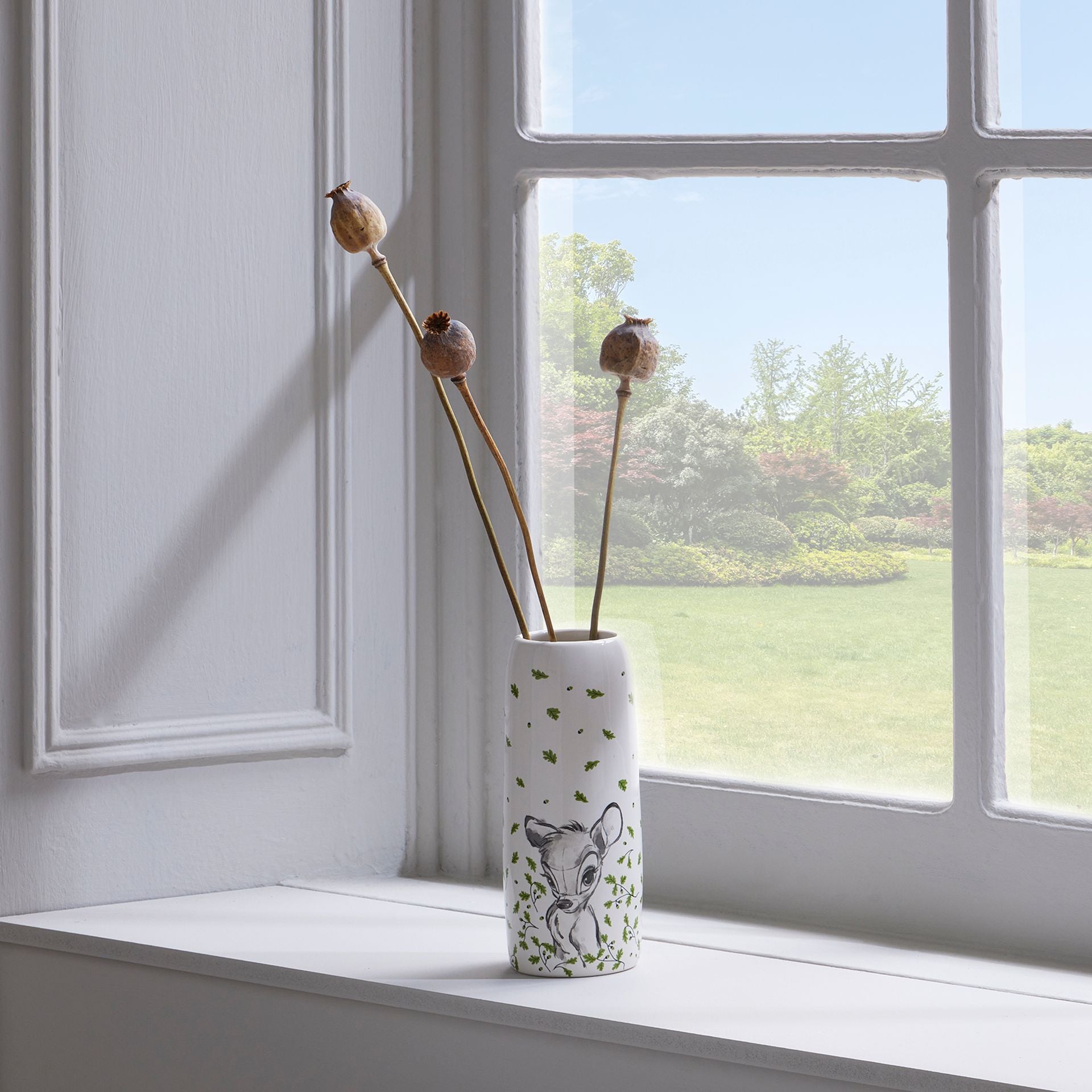 Vase with a deer design on a windowsill with dried plants, window in the background