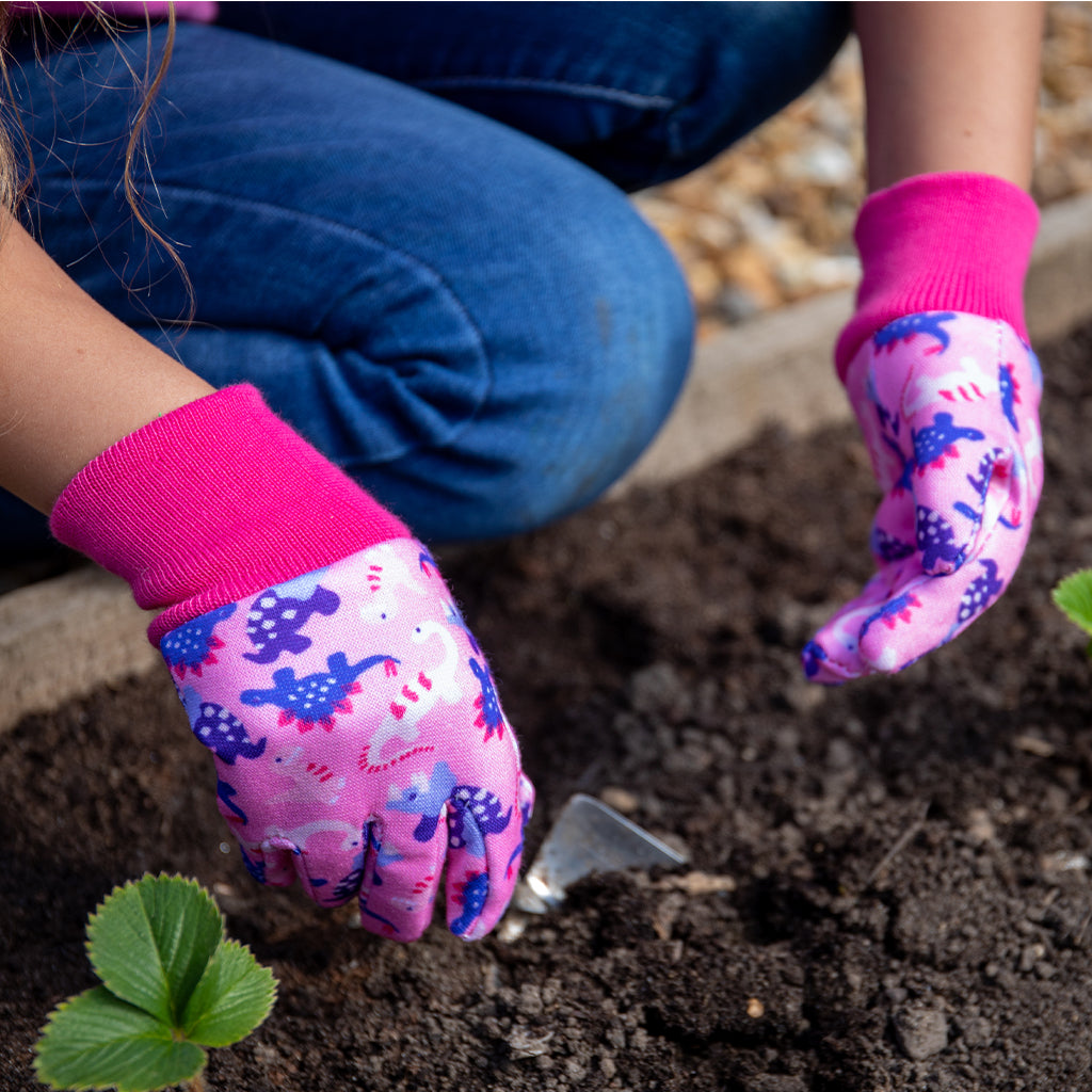 Person wearing pink gardening gloves with animal prints, planting a small plant in soil.