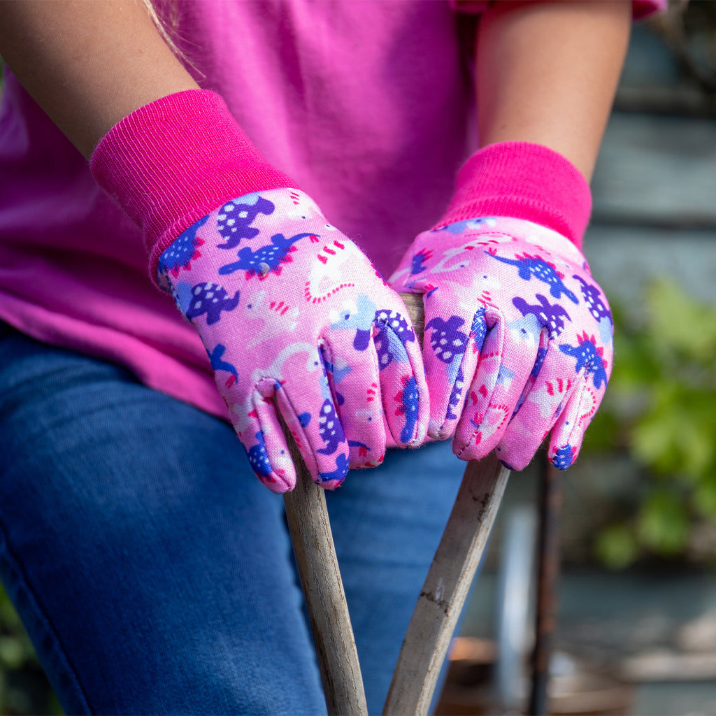 Child wearing pink gardening gloves with dinosaur design holding two small plants.