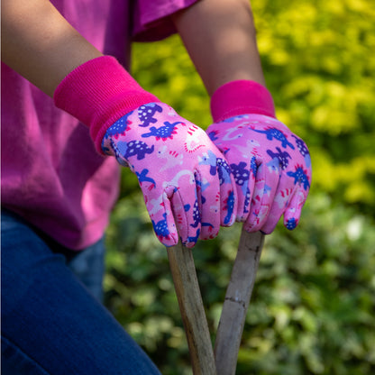 Person wearing pink gardening gloves with floral pattern holding a tool against a green background