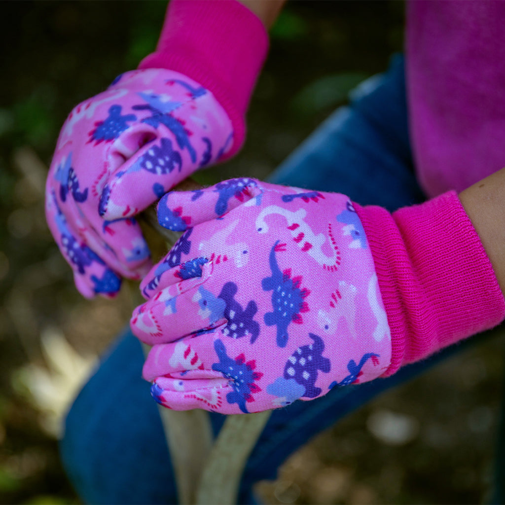 Pink gardening gloves with dinosaur pattern worn by a child outdoors