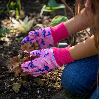 Person wearing pink gardening gloves with floral pattern tending to plants in a garden.