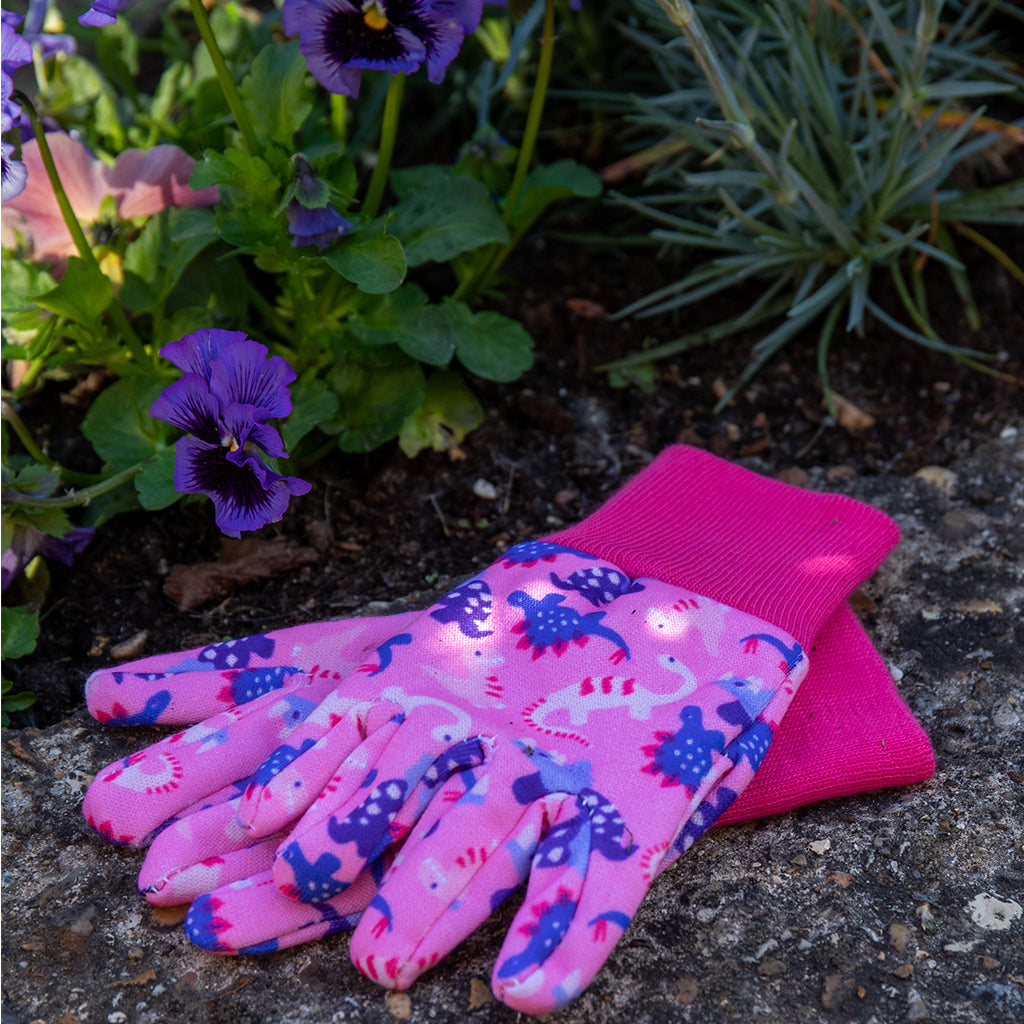 Pink gardening gloves with dinosaur pattern on a garden background