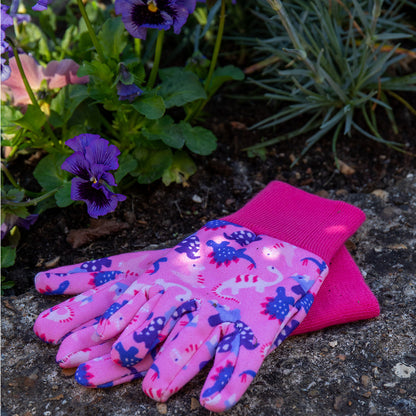 Pink gardening gloves with dinosaur pattern on a garden background