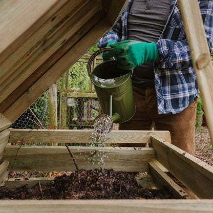 Filled wooden compost bin being watered with a watering can