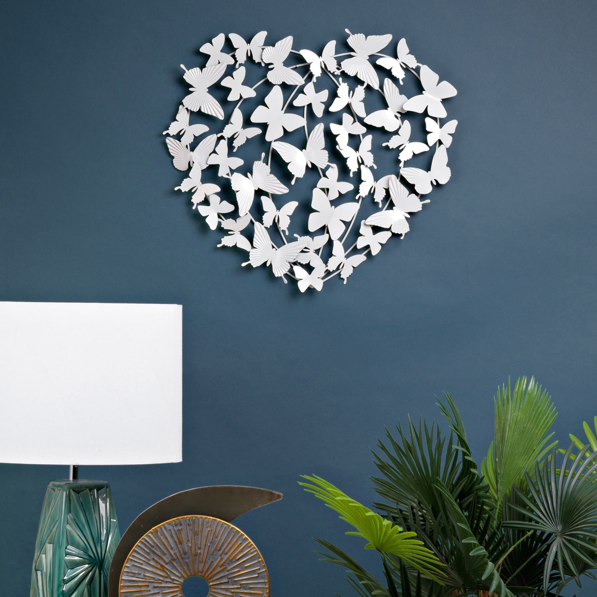 Heart-shaped wall decor made of white butterflies on a blue wall with a lamp and plants.
