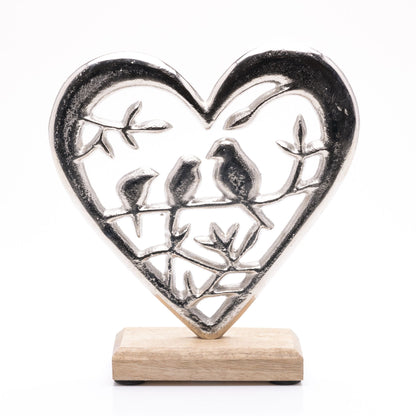 Decorative heart-shaped metal sculpture with birds on a wooden base against a white background