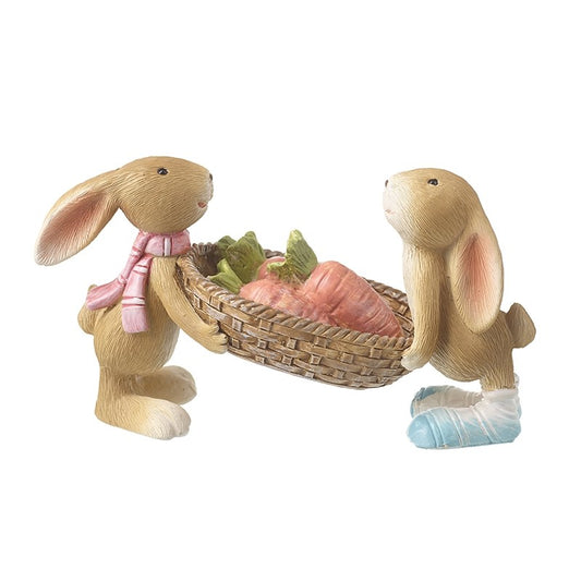 Two rabbit figurines with a basket of carrots and vegetables on a white background