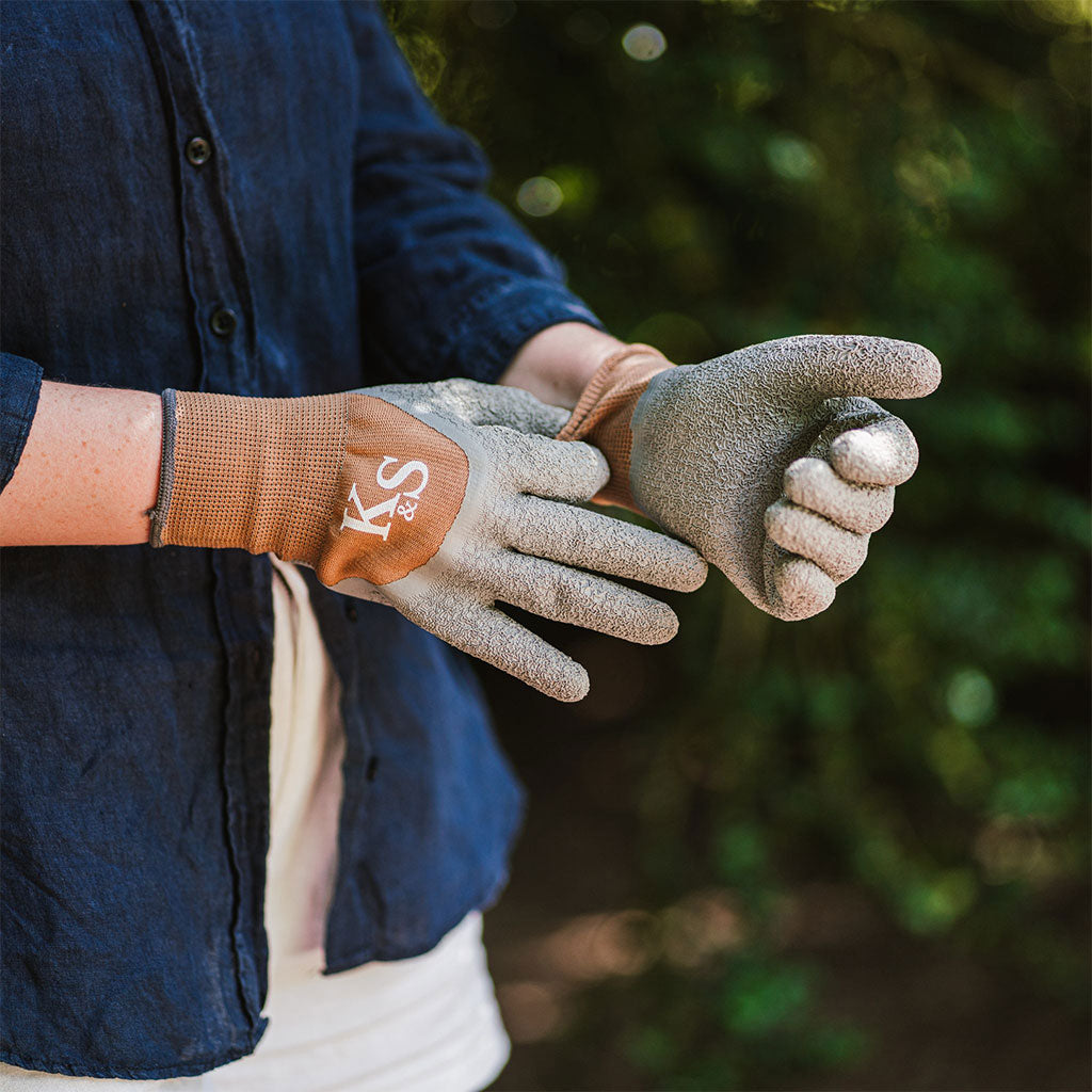 Person wearing gardening gloves with a brand logo, outdoors.