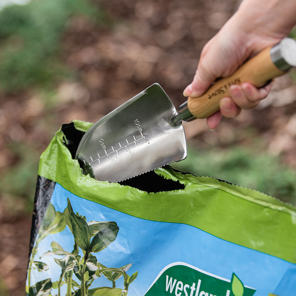 Person using a trowel to open a Westland plant food bag outdoors.