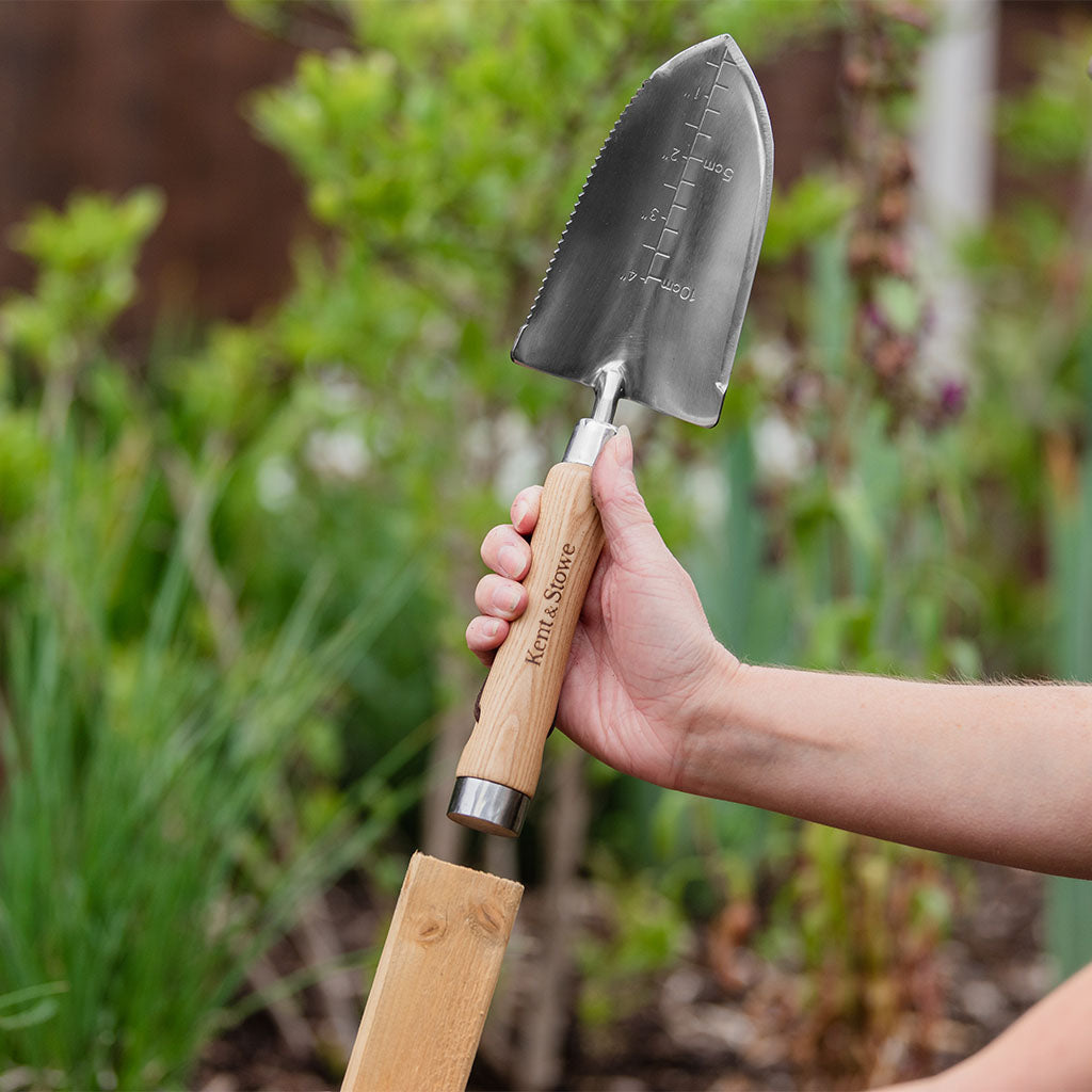 Gardening trowel with wooden handle held by a person in a garden setting