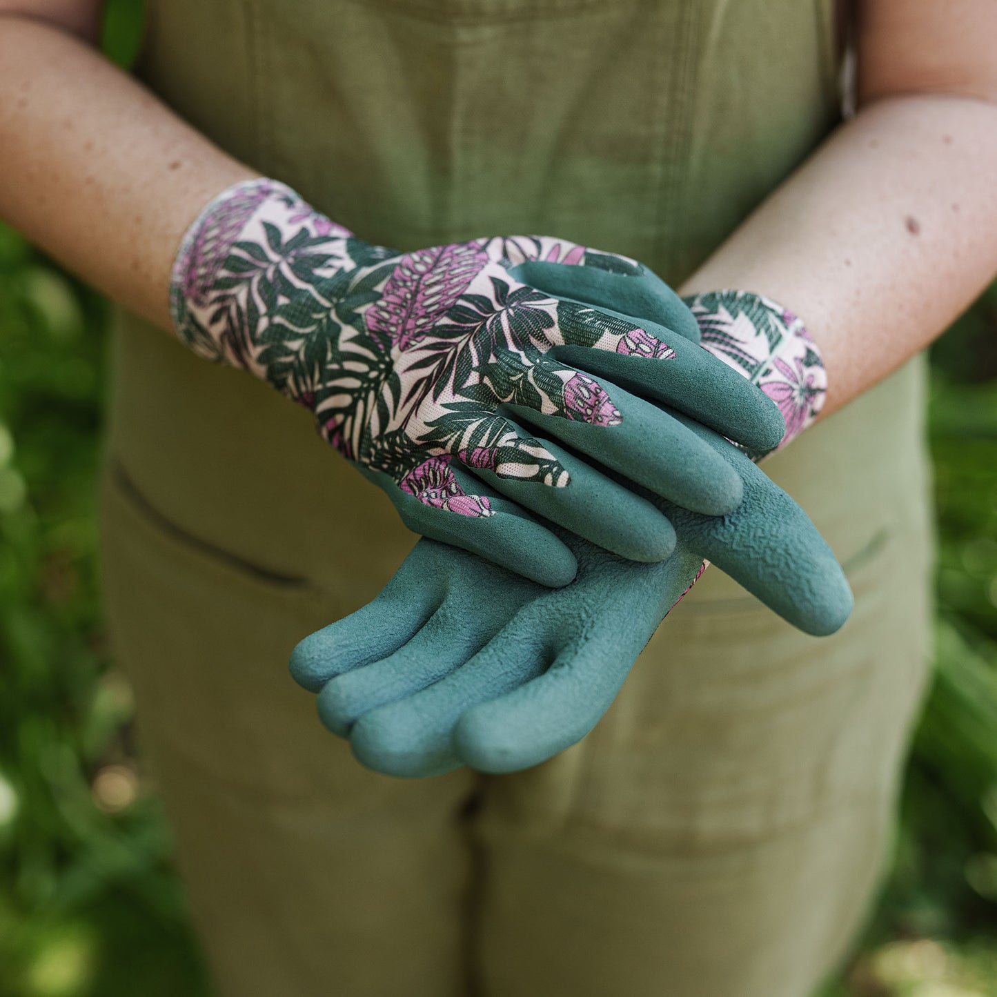 Person wearing teal gardening gloves with floral pattern in a garden setting