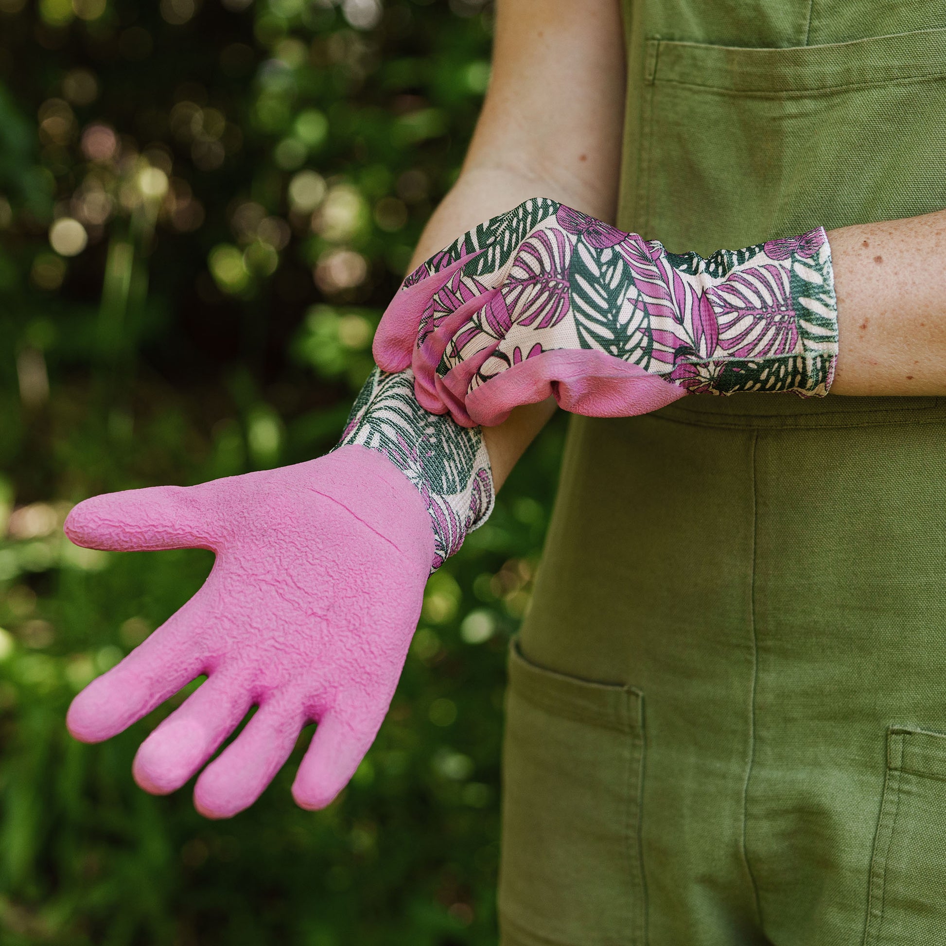 Person wearing pink gardening gloves with a patterned cuff against a green background