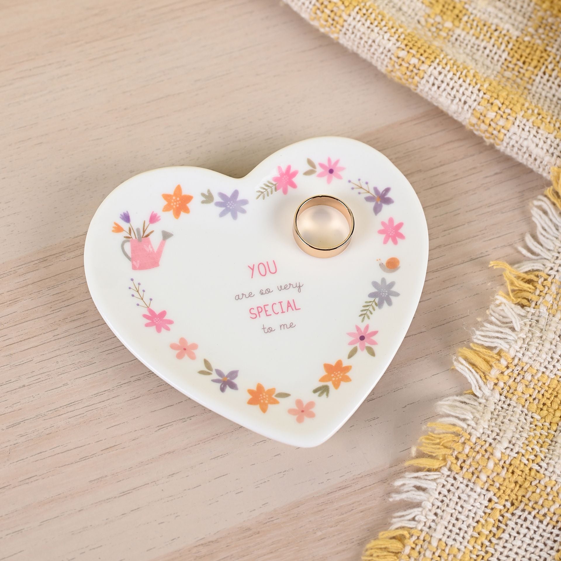 Heart-shaped decorative plate with floral designs and a ring on a wooden surface