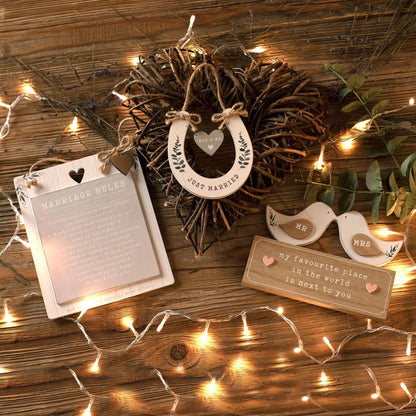 Decorative items including a wreath, hanging heart sign, and 'Mr' and 'Mrs' signs on a wooden surface with string lights.