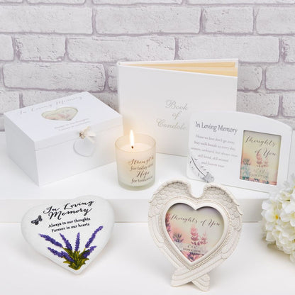 Memorial items including a candle, heart-shaped photo frame, and engraved stone on a white surface with a brick wall background.