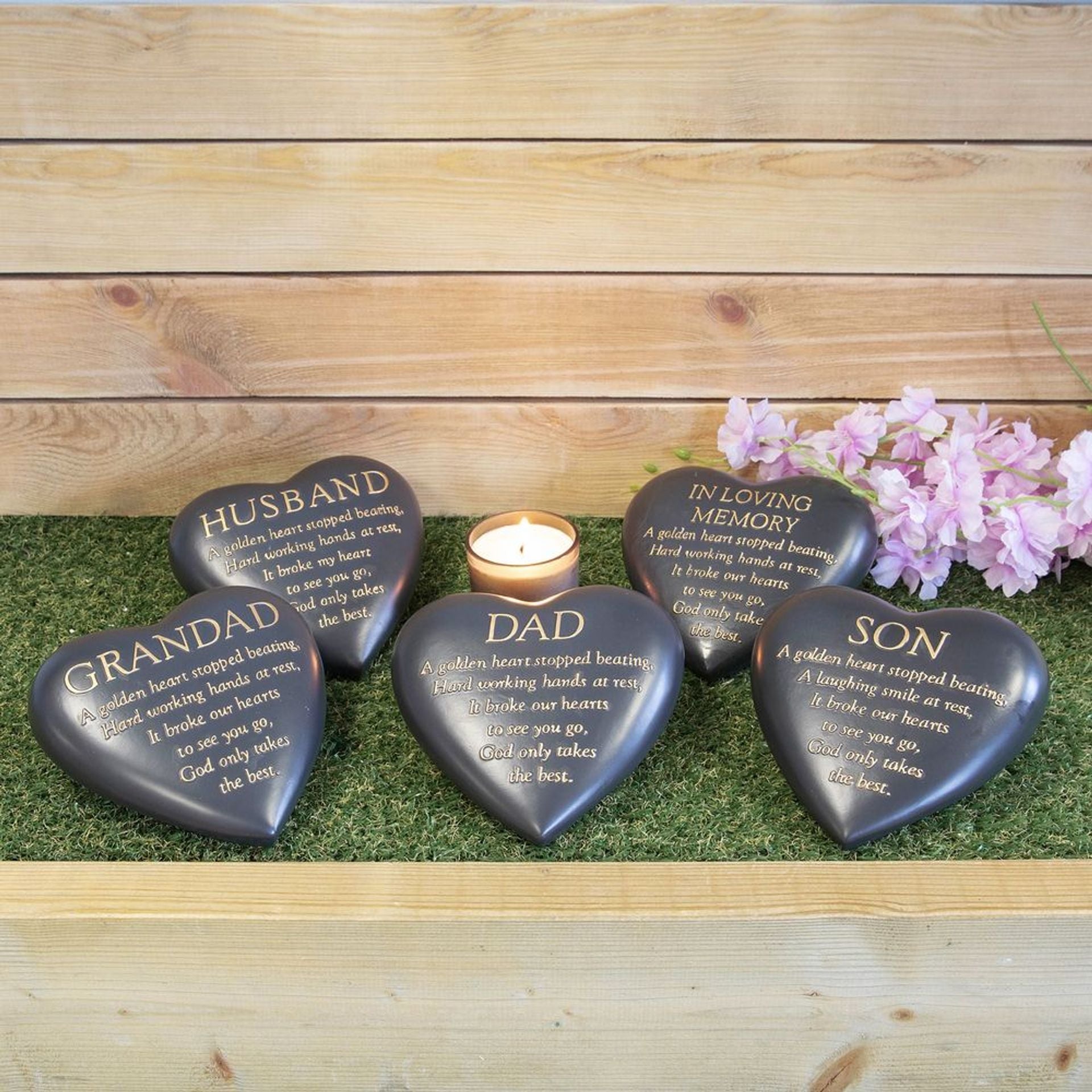Heart-shaped memorial stones with engravings on a wooden surface with flowers