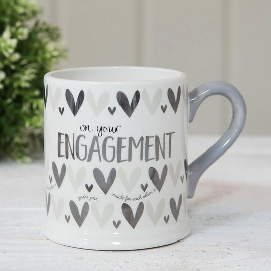Mug with 'on your engagement' text and heart patterns on a light surface.