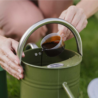 Person pouring liquid into a green metal bucket with a handle.