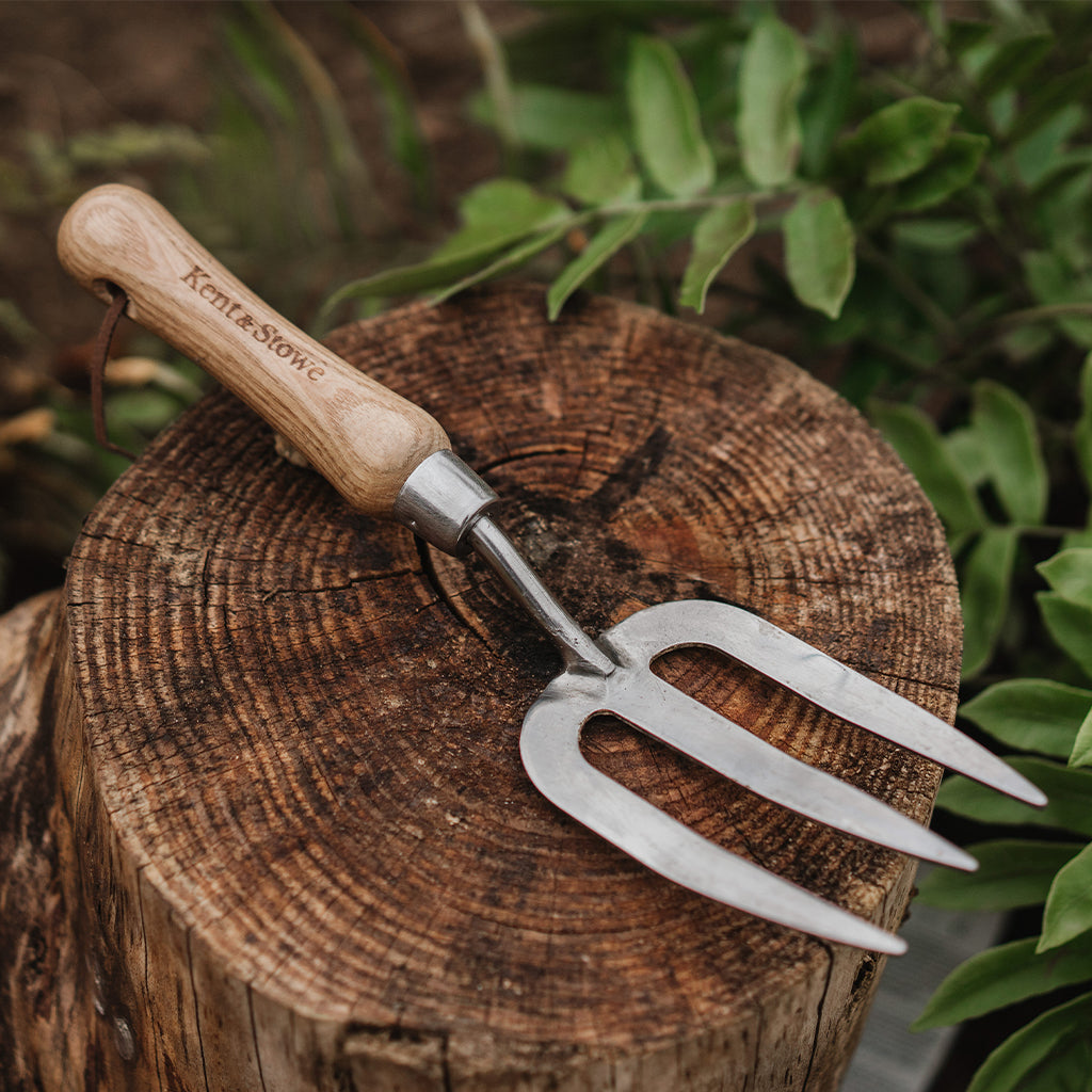 Gardening fork with wooden handle on a wooden log surrounded by greenery