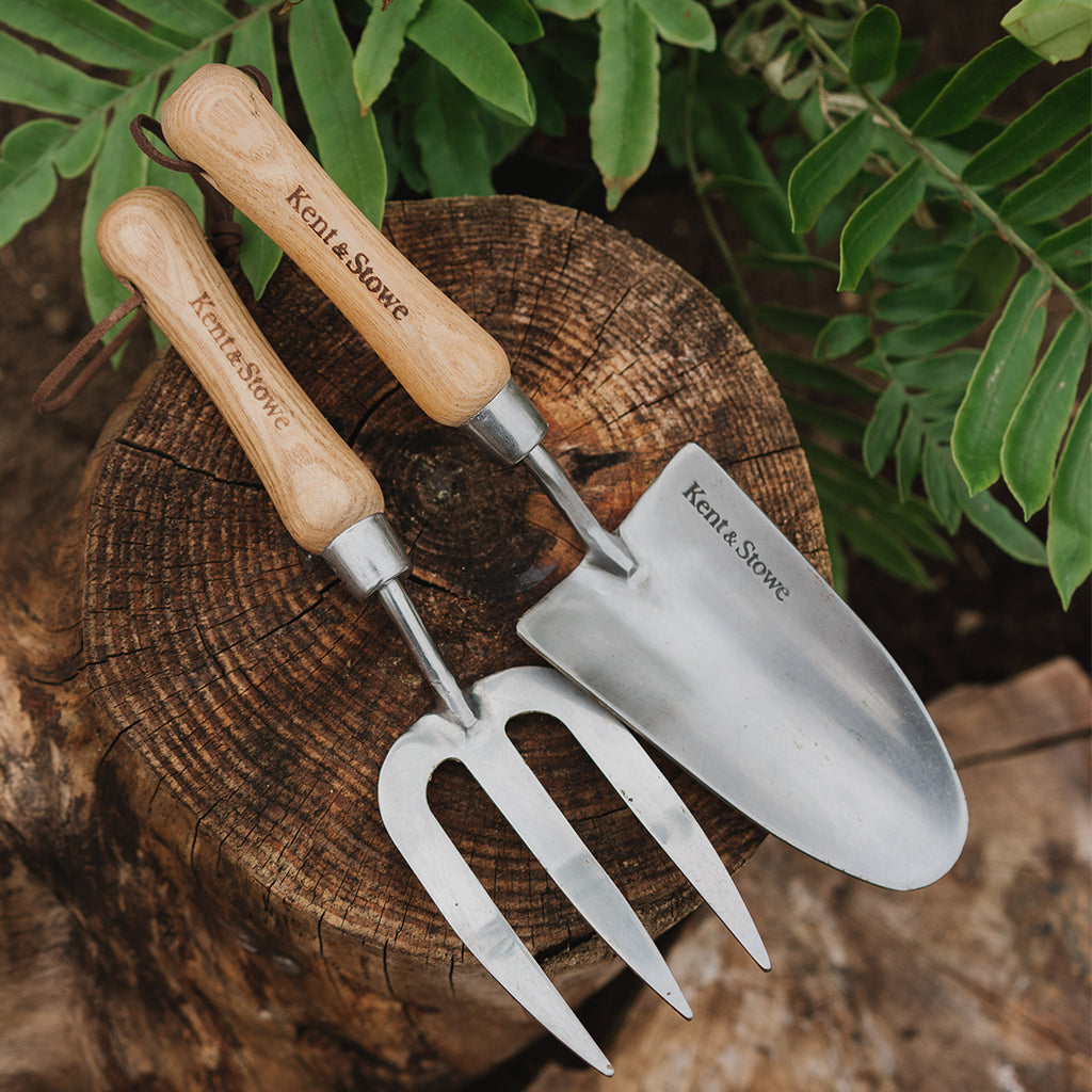 Gardening tools with wooden handles on a wooden stump with green foliage in the background
