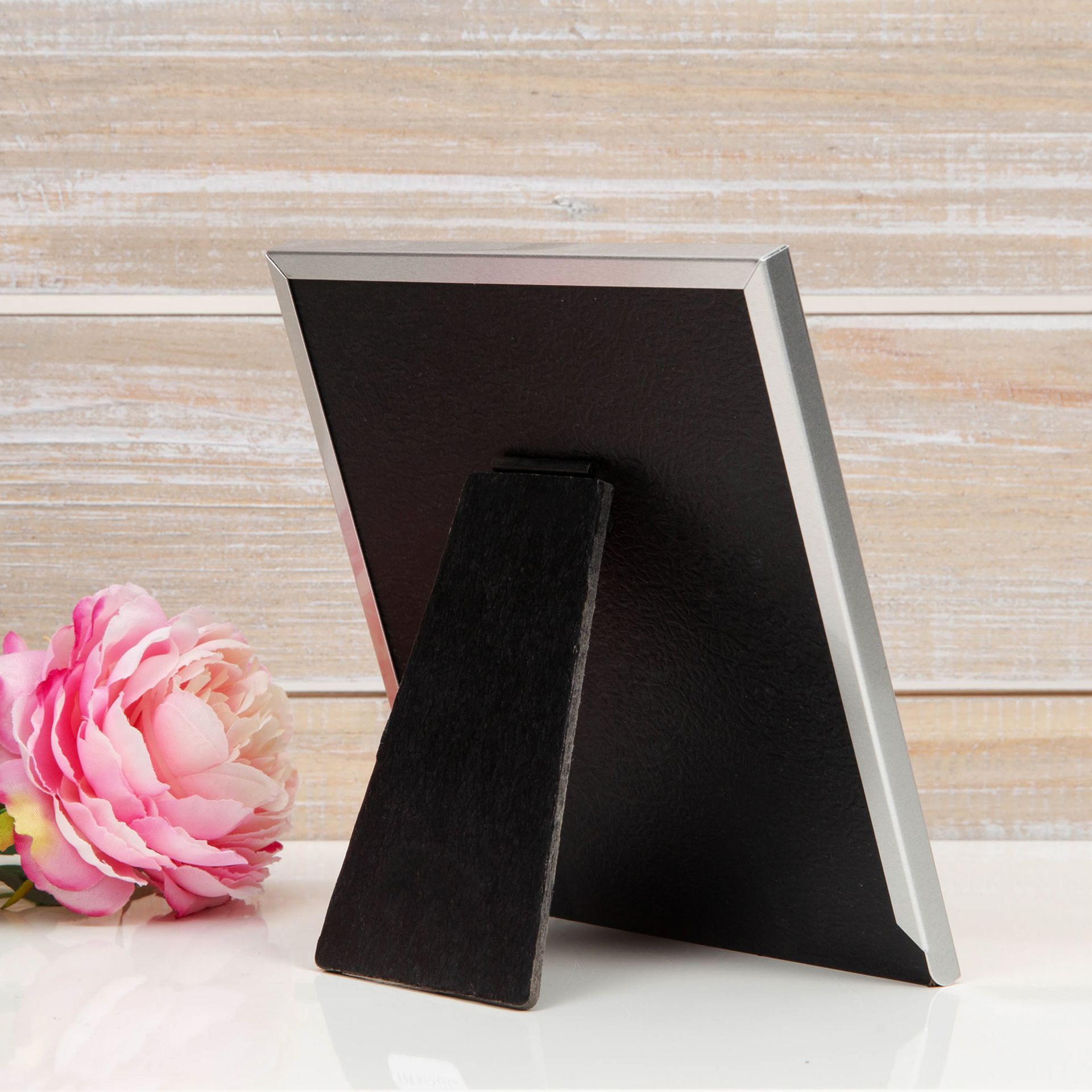 Black photo frame with a pink flower on a wooden surface