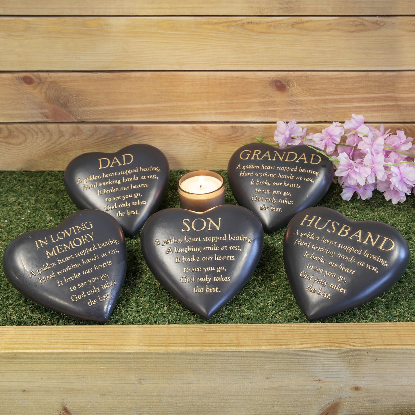 Heart-shaped memorial stones with engraved text on a grassy surface with a wooden background.
