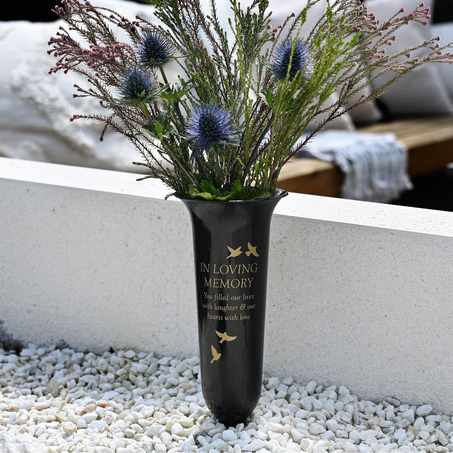 Vase with flowers labeled 'In Loving Memory' on a pebbled surface.