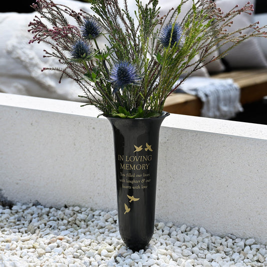 Vase with flowers labeled 'In Loving Memory' on a pebbled surface.