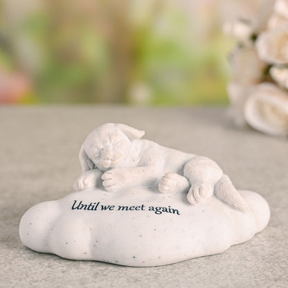 White figurine of a cat lying on a rock with 'Until we meet again' text, placed on a surface with a blurred natural background.