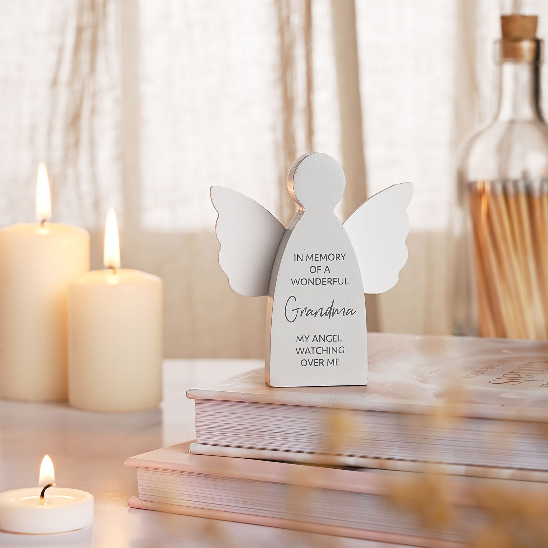 White angel figurine with engraved text on a table with candles and books.
