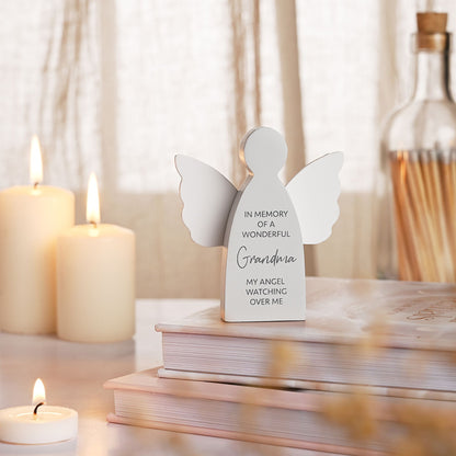White angel figurine with engraved text on a table with candles and books.