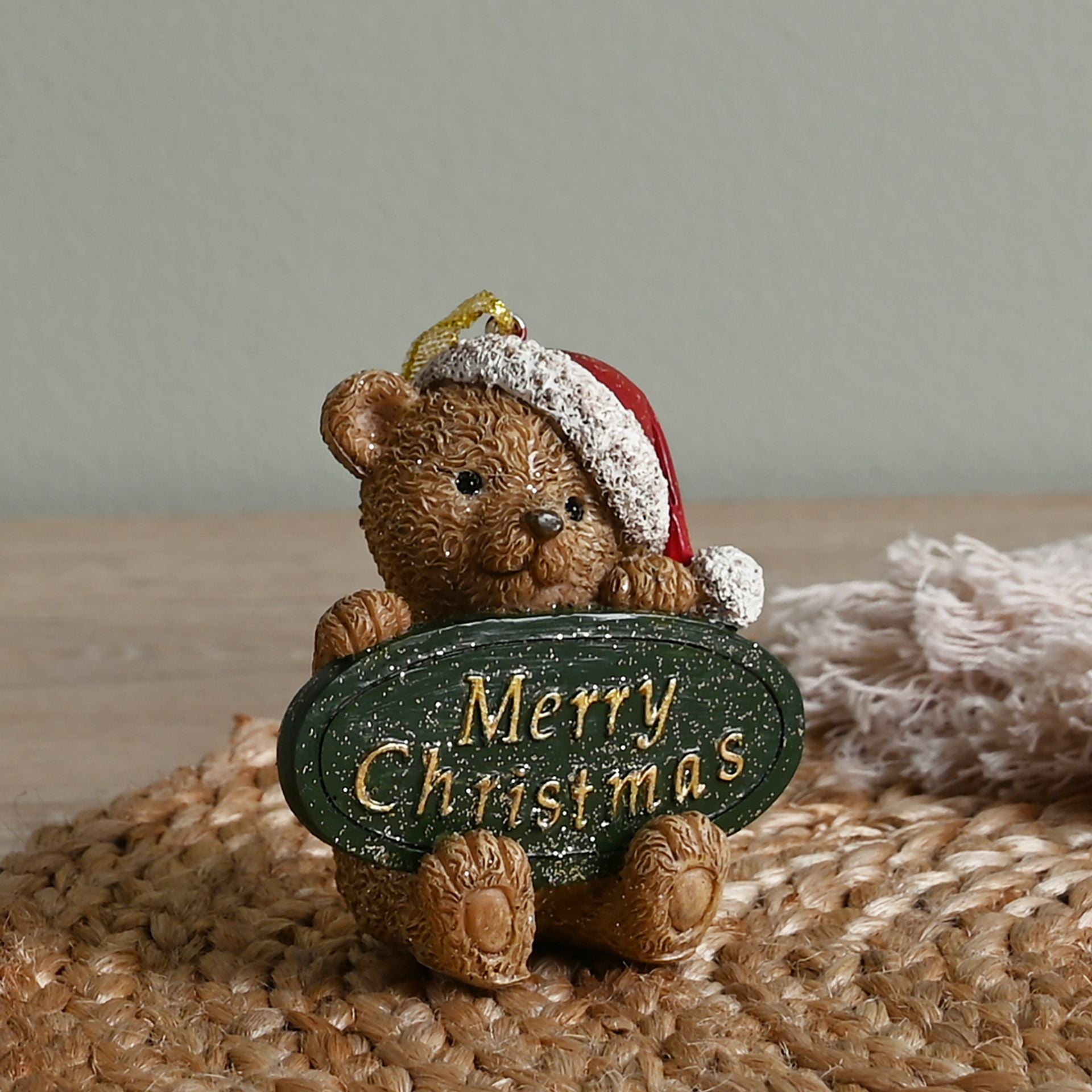 Teddy bear wearing a Santa hat holding a 'Merry Christmas' sign on a textured surface.