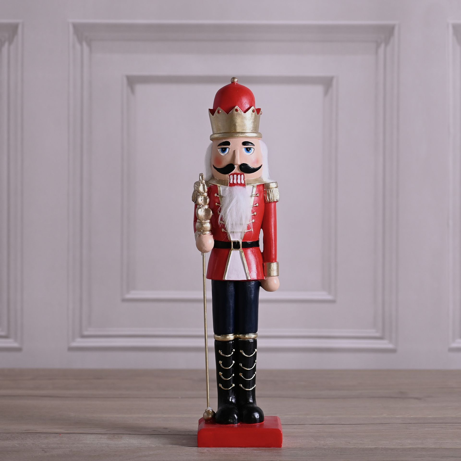 Decorative nutcracker figure with red outfit and crown on a wooden floor.