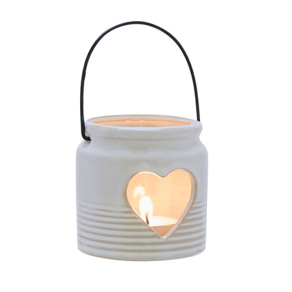 White ceramic lantern with a heart-shaped cutout and a lit candle inside on a white background