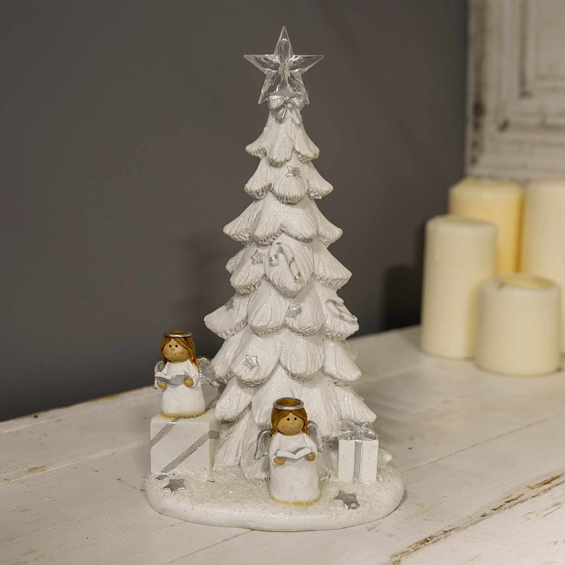 Decorative Christmas tree with star on top, two angel figures, and presents on a white surface.