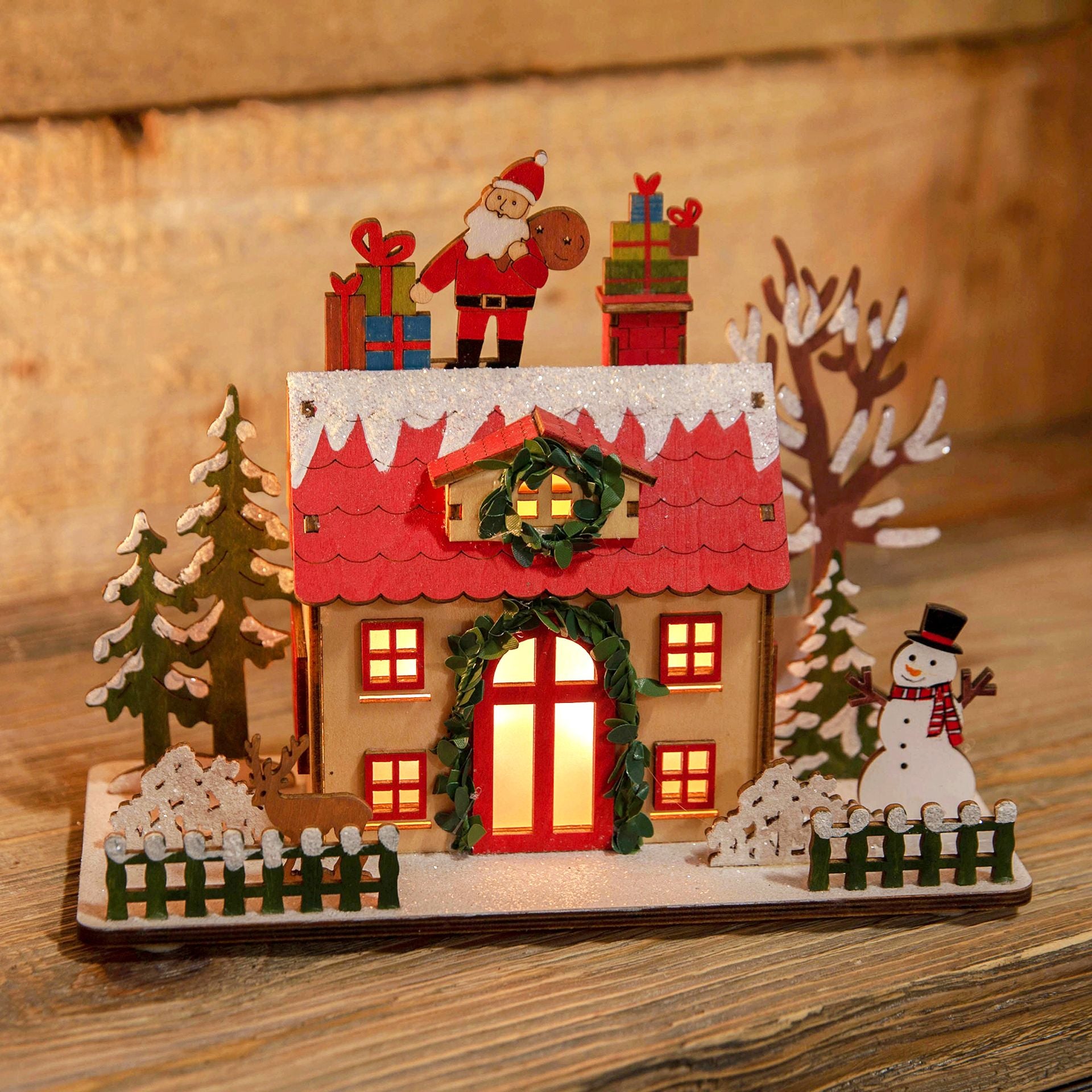 Decorative Christmas scene with a house, Santa Claus, and snowman on a wooden surface.