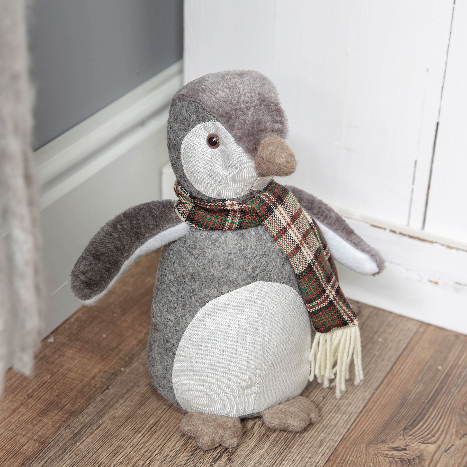 Stuffed penguin toy with a scarf on a wooden floor.