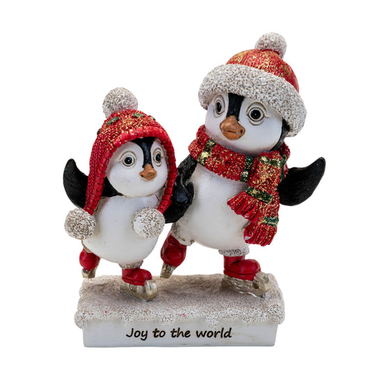 Two penguin figurines wearing festive hats and scarves with 'Joy to the world' text on a white background.